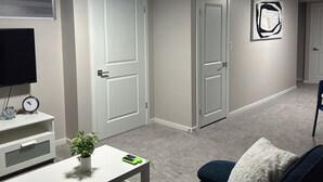 Un couloir avec des portes blanches, un téléviseur à écran plat, une horloge et une petite table sur laquelle est posée une plante.
