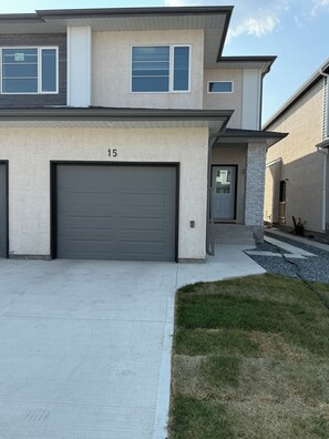 A two-story house with a garage, a driveway, and a well-maintained lawn. - One-BR Private Suite in South Winnipeg | Near UofM (STRA-2025-2655115) (Winnipeg)