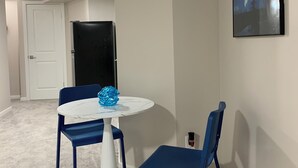 Une pièce avec une table ronde blanche, deux chaises bleues, un objet décoratif bleu posé sur la table, une porte noire et un tableau encadré au mur.