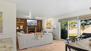 A living room with a fireplace, a sofa, a dining table, and a view of the outdoors. - The Timberline House | Modern Mountain Comfort | Walk to Town & Near Lifts (Ketchum)