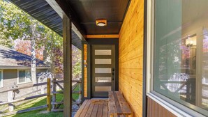 A wooden exterior with a bench and a door, a wooden fence, and a grassy area. - The Timberline House | Modern Mountain Comfort | Walk to Town & Near Lifts (Ketchum)
