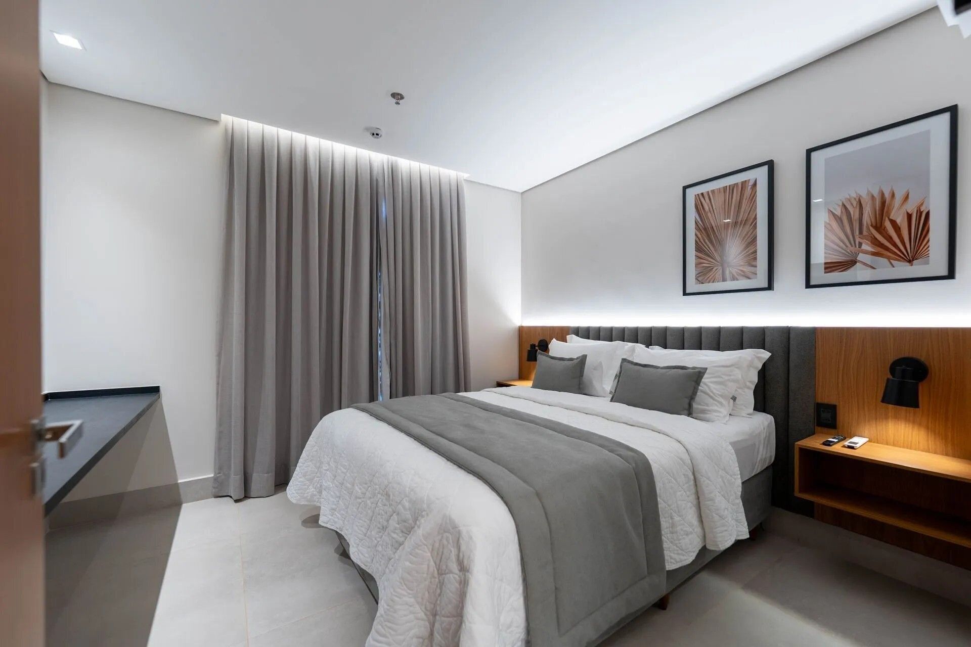 Quarto de hotel moderno com uma cama grande, uma mesa de cabeceira e duas obras de arte emolduradas na parede.