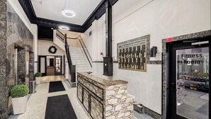 Een hotel lobby met een marmeren trap, een bordje voor de fitnessruimte en een receptiebalie.