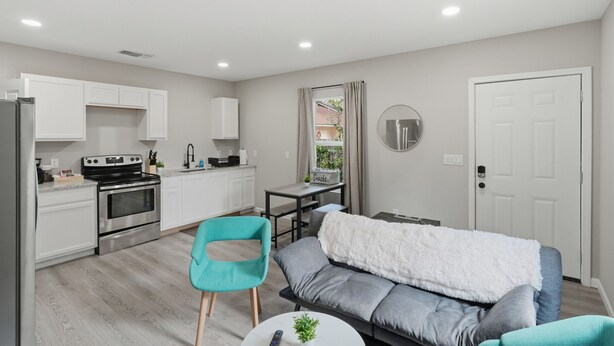 Une cuisine moderne avec des meubles blancs, une cuisinière noire et une table à manger avec une chaise.