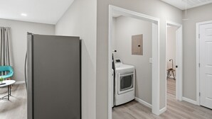 Un appartement moderne avec un réfrigérateur gris, un lave-linge et un coin repas agrémenté d’une chaise turquoise.