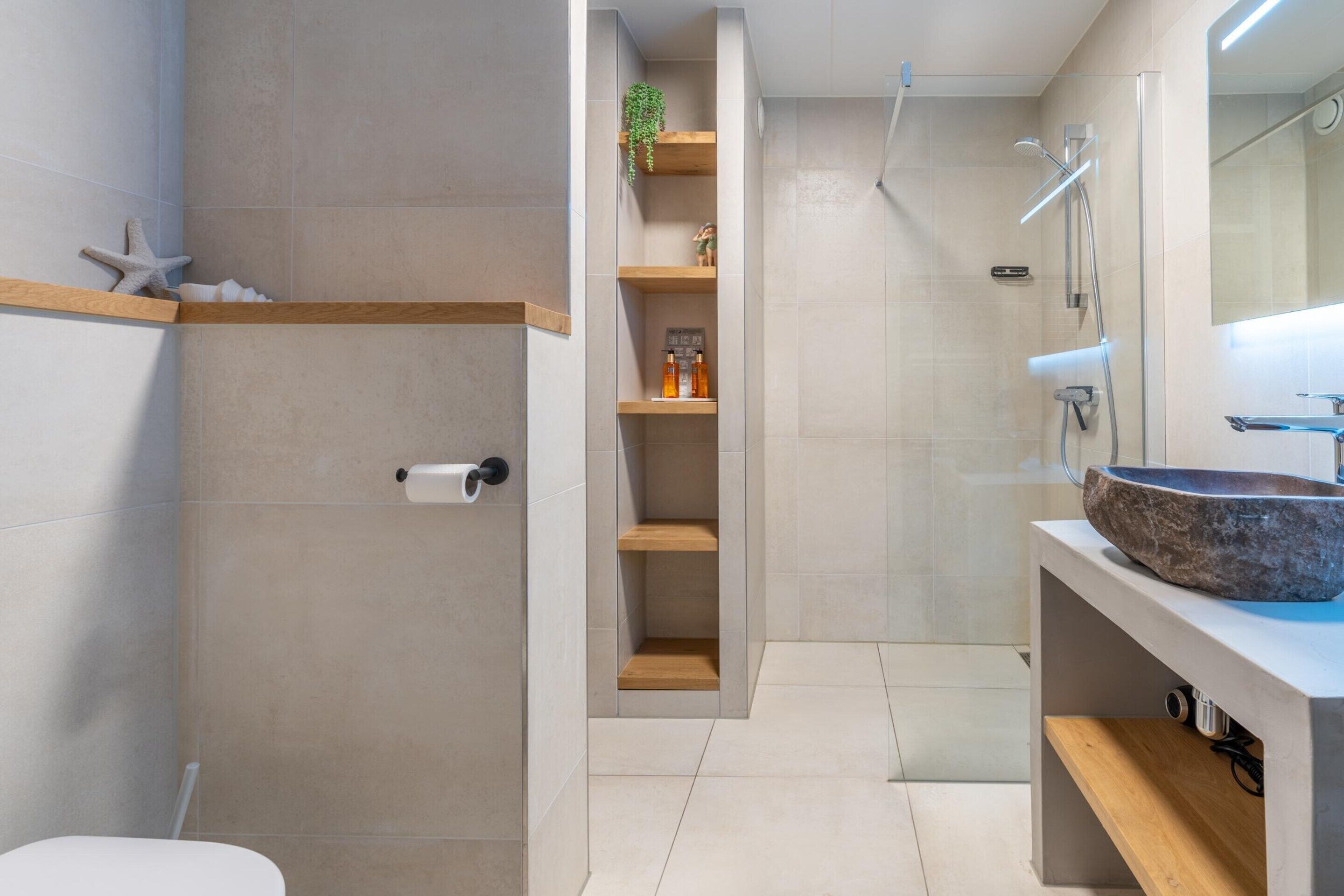 A modern bathroom with a built-in shower, a wooden shelf with toiletries, and a large mirror above the sink.