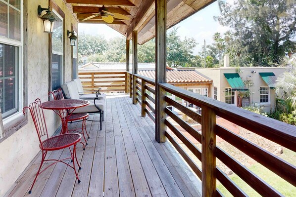 A wooden deck with a railing, a table, and two chairs. - Charming Garage Apartment Near Restaurants, Bars and Historic Downtown (St. Augustine)