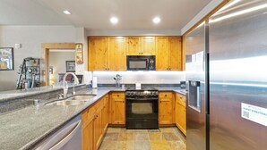 Una cocina moderna con encimeras de granito, armarios de madera, un refrigerador de acero inoxidable y un horno empotrado.