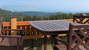 Una terraza de madera con una mesa y sillas, con vistas a un valle boscoso y montañas distantes.