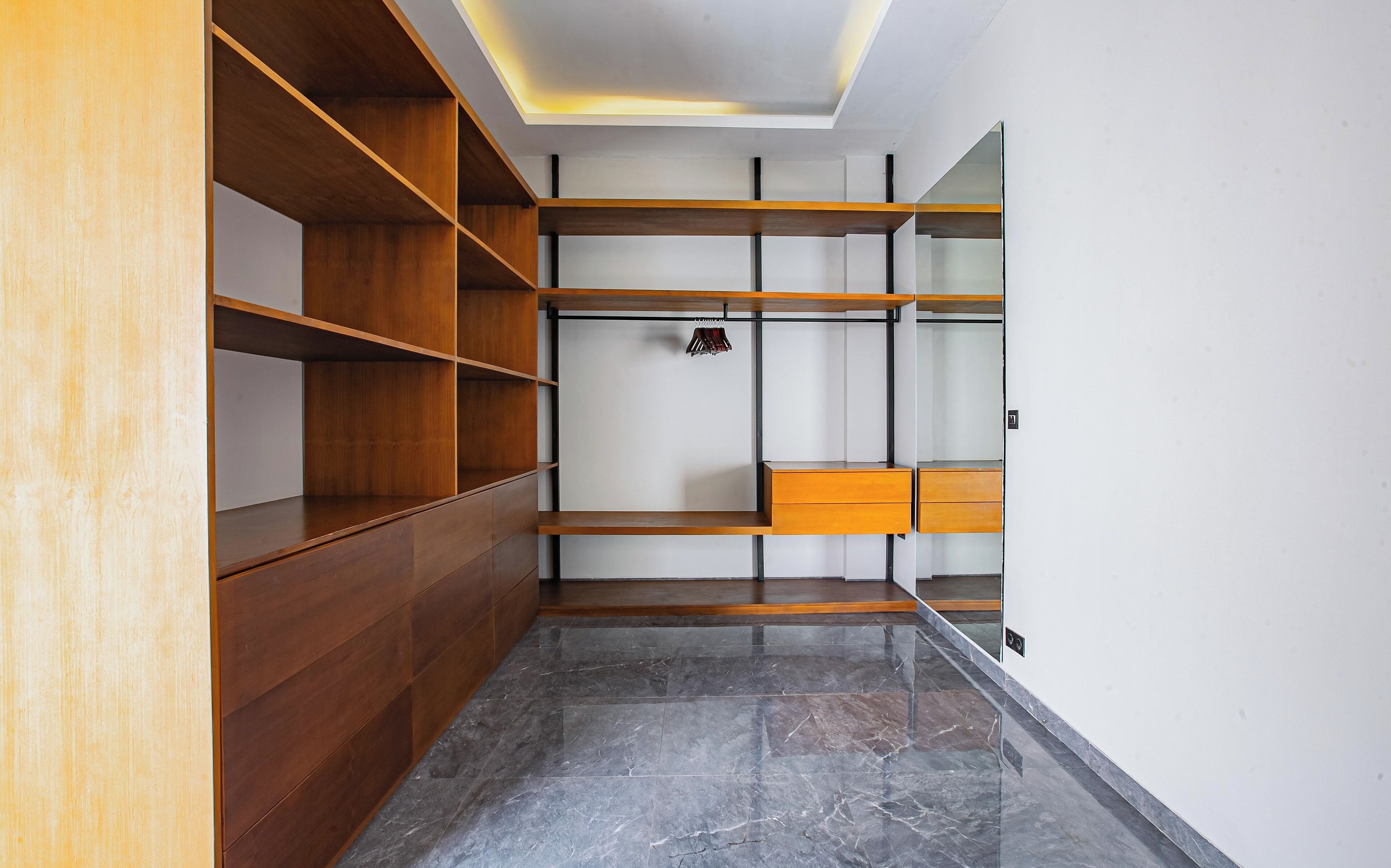 A modern closet with wooden shelves and drawers, a marble floor, and a ceiling light.