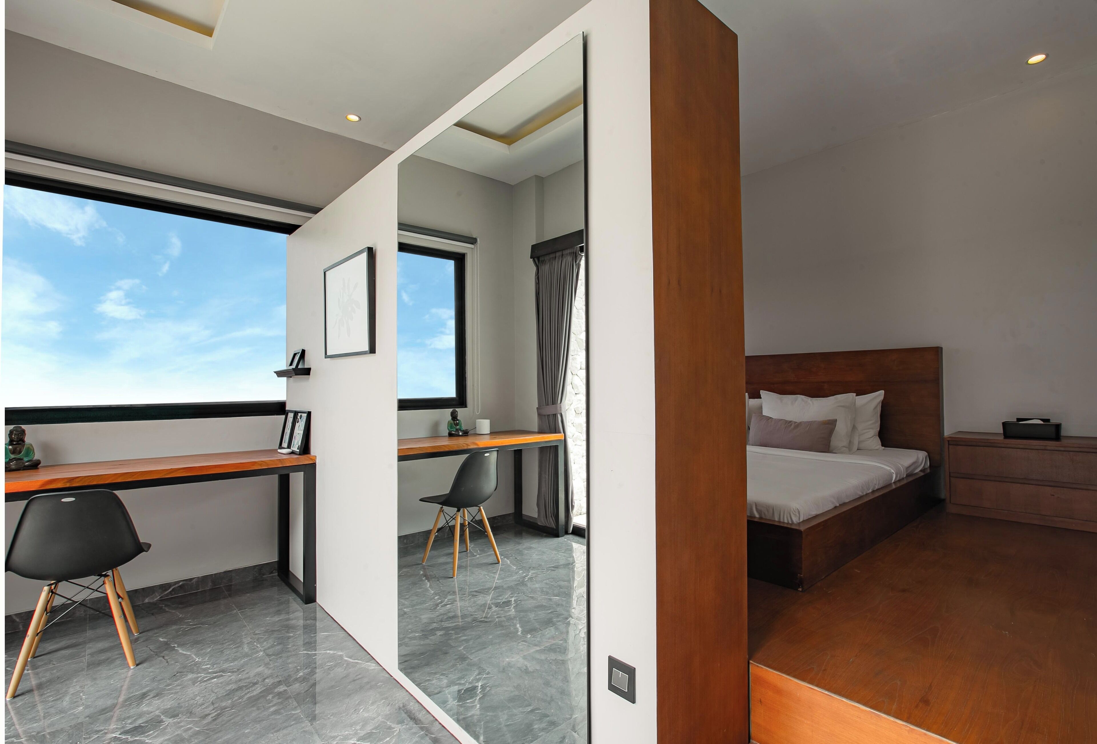 Una habitación de hotel moderna con un escritorio de madera, una cama y un ventanal grande.