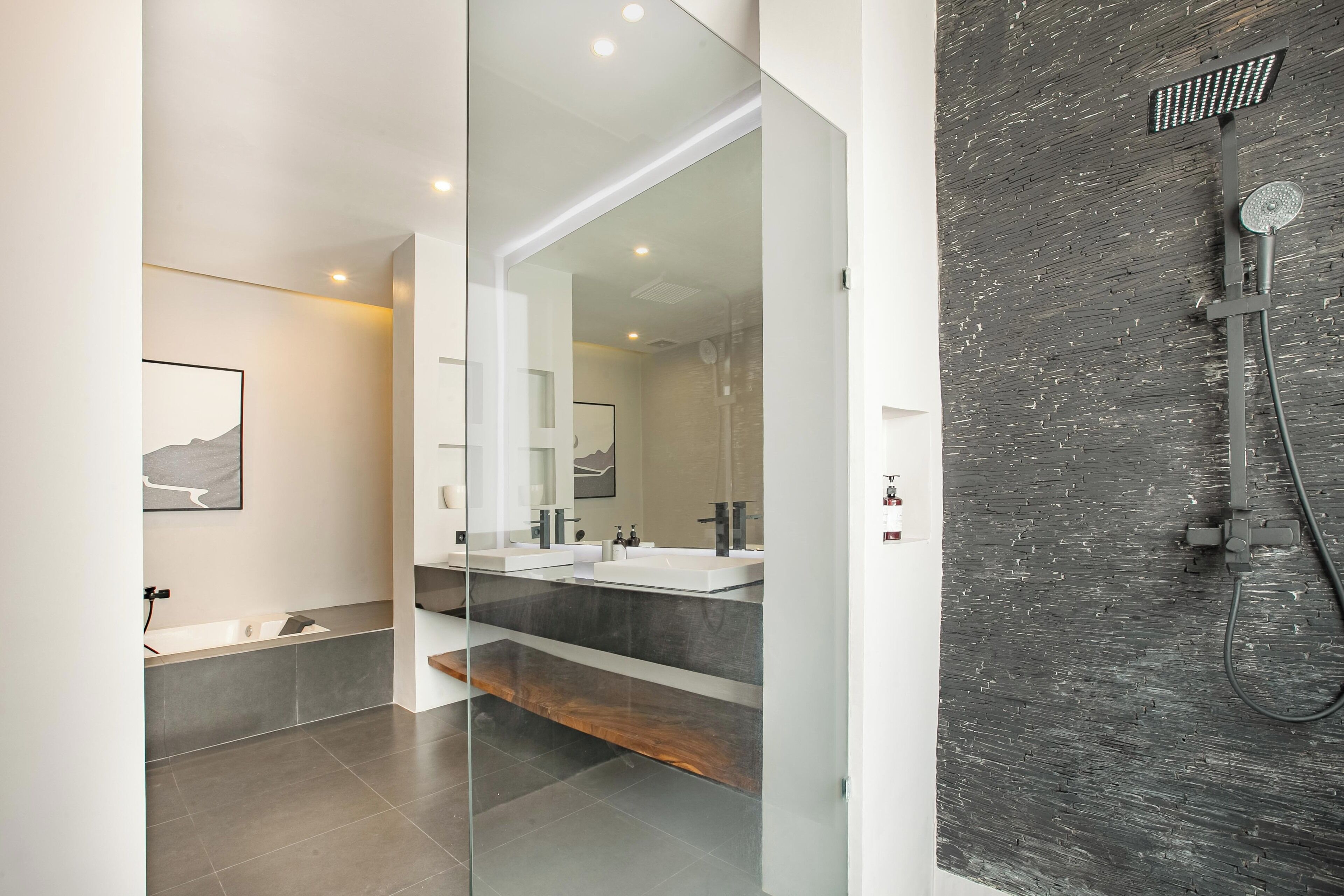 A modern bathroom with a glass partition, a large mirror, a shower with a rain showerhead, and a wooden shelf.