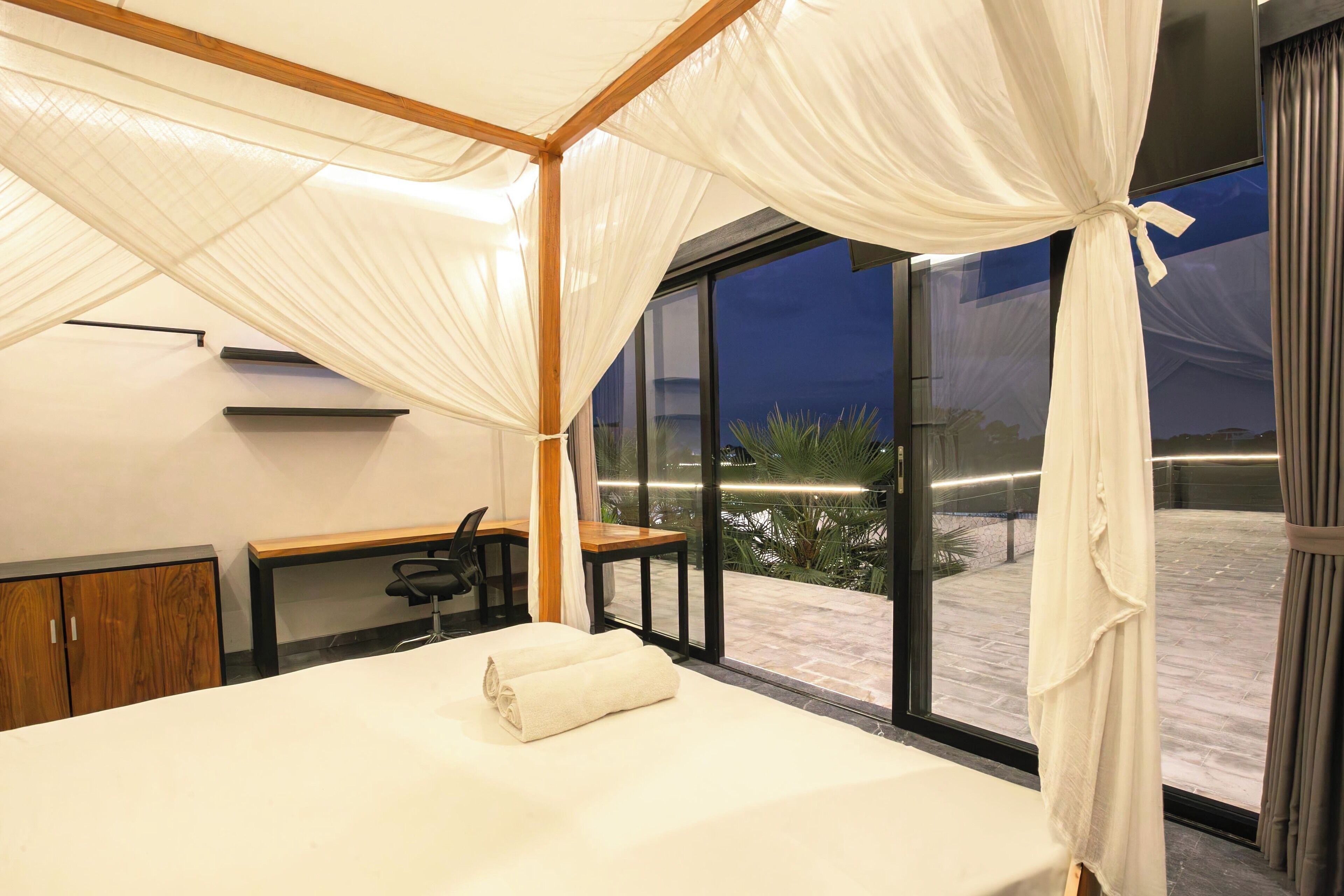 A bedroom with a canopy bed, a desk, and a view of the outdoors.