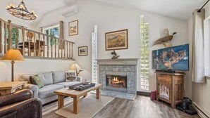 A spacious living room with a fireplace, a television, and a staircase leading to another level. - New! Large Patio, Dogs Allowed, Great Location! (Whitefish)