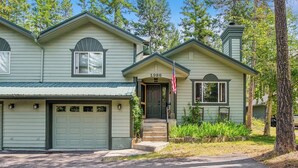 A two-story house with a garage, a front porch, and a small attached shed. - New! Large Patio, Dogs Allowed, Great Location! (Whitefish)