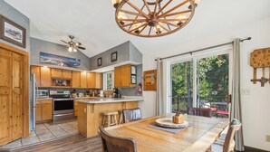 A spacious kitchen with wooden cabinets, a central island, and a dining area with a large wooden table and chairs. - New! Large Patio, Dogs Allowed, Great Location! (Whitefish)