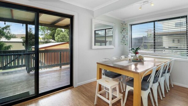 A dining area with a wooden table and chairs, large windows with blinds, and a view of the outdoors. - Lakeview Retreat Bonnie Doon - Sleeps 11 (Bonnie Doon)