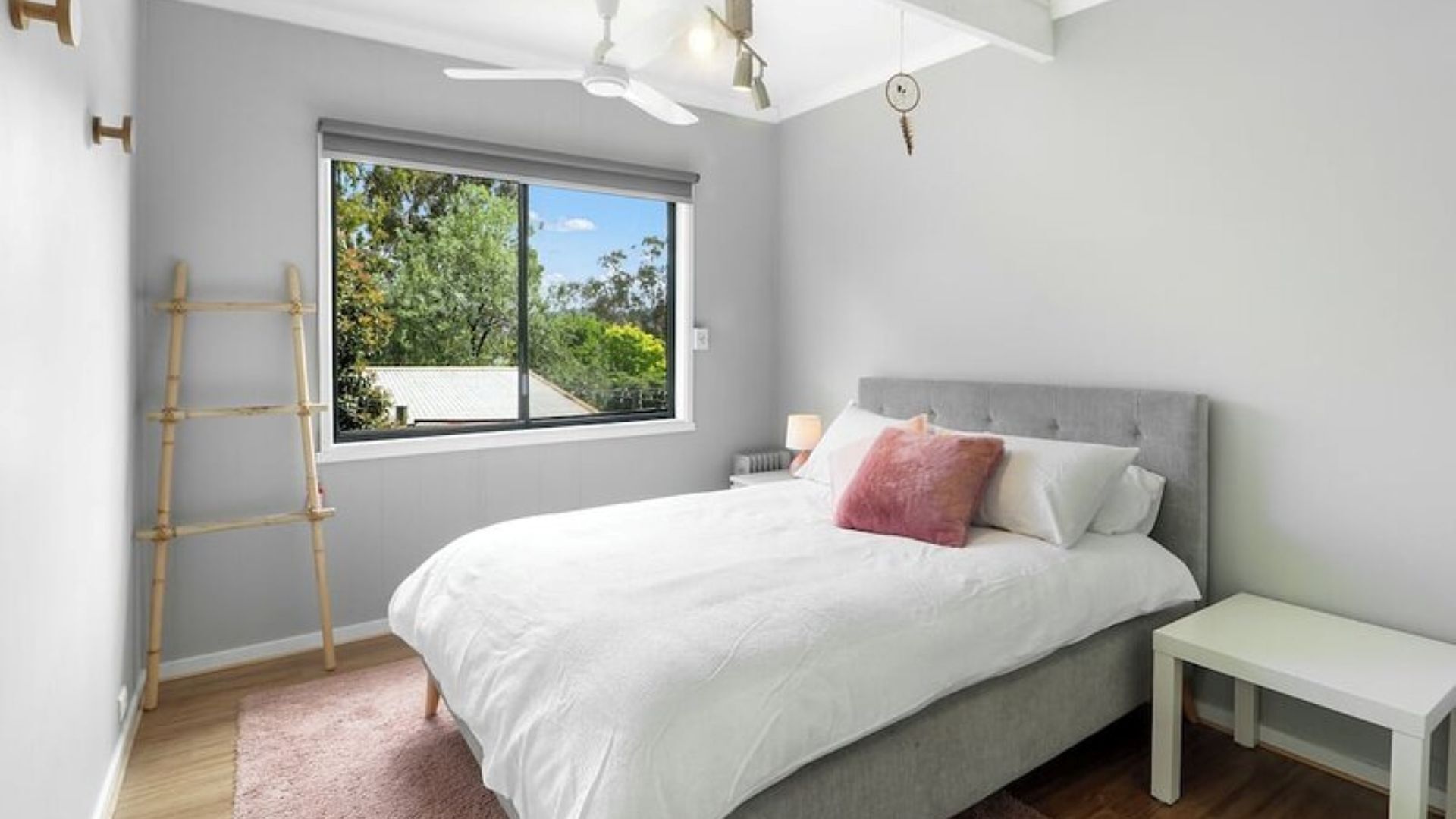 A bedroom with a bed, a window, a ceiling fan, and a bedside table.