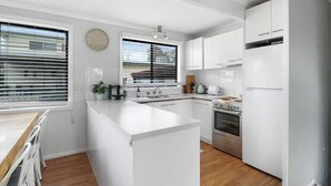 A modern kitchen with white cabinetry, a central island, a built-in oven, and a large window with blinds. - Lakeview Retreat Bonnie Doon - Sleeps 11 (Bonnie Doon)