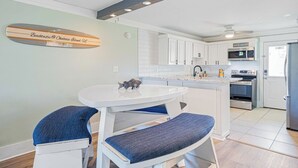 Een moderne keuken met witte kasten, een inbouwoven en een magnetron. Er is een ronde witte tafel met blauwe stoelen met kussens.