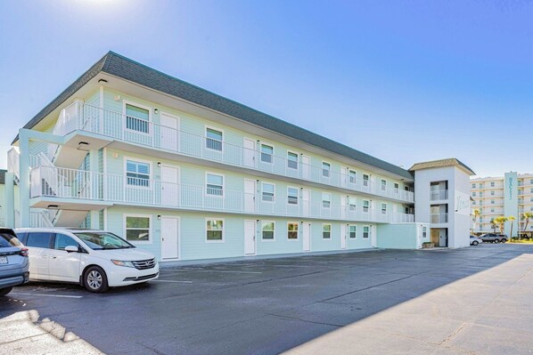 Un motel à plusieurs étages, à la façade bleu clair, doté de balcons et d’un parking.