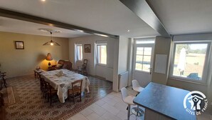 Ein Essbereich mit einem Tisch für vier Personen, einer Couch und einem gemusterten Teppich. Zwei Fenster sorgen für natürliches Licht.