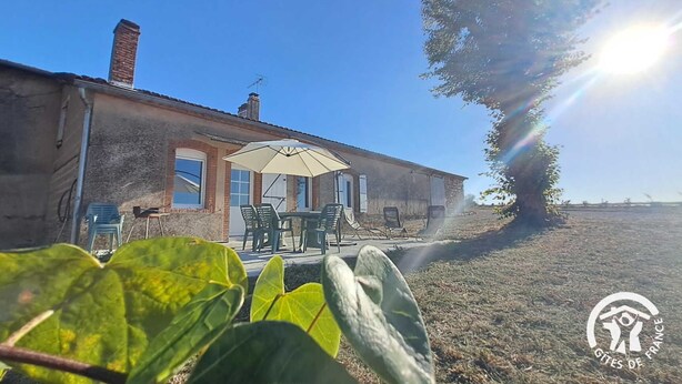 Ein rustikales Gebäude mit Terrasse, Sitzgelegenheiten im Freien und einem großen Sonnenschirm.
