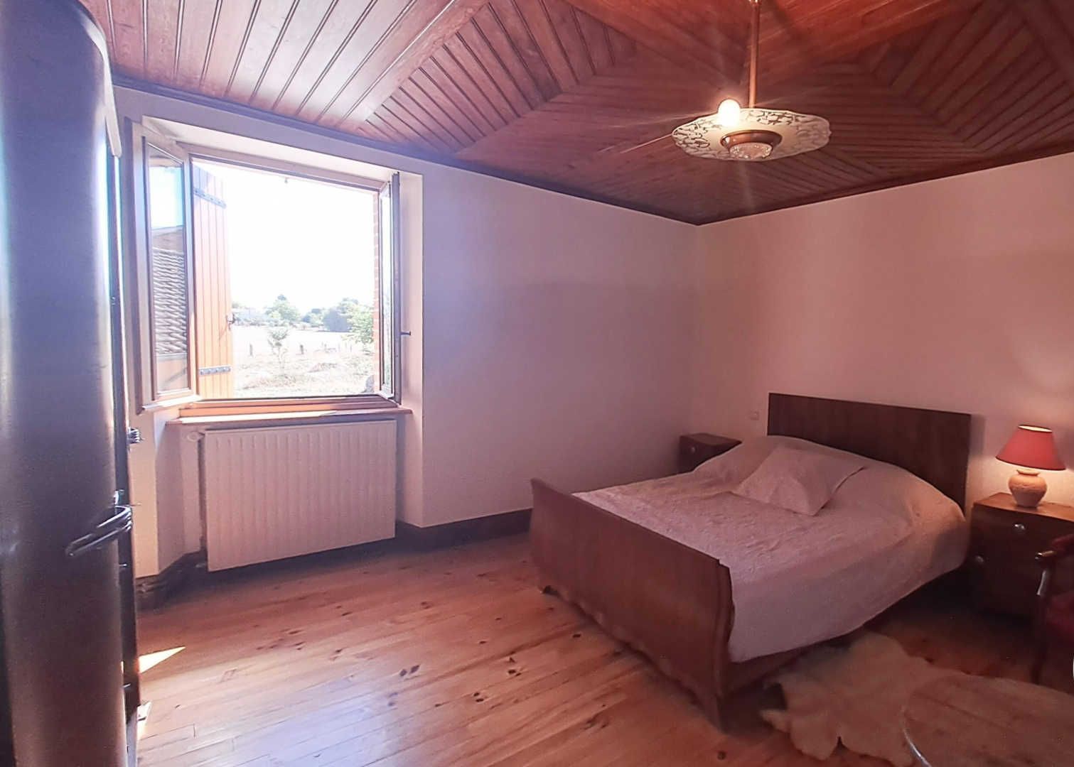 A bedroom with a wooden bed, a nightstand with a lamp, a window with blinds, and a radiator.