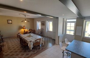 A dining area with a table set for four, a sofa, and a patterned rug. There are two windows providing natural light.
