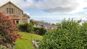 A historic building with a prominent arched entrance, surrounded by lush greenery and a coastal view.