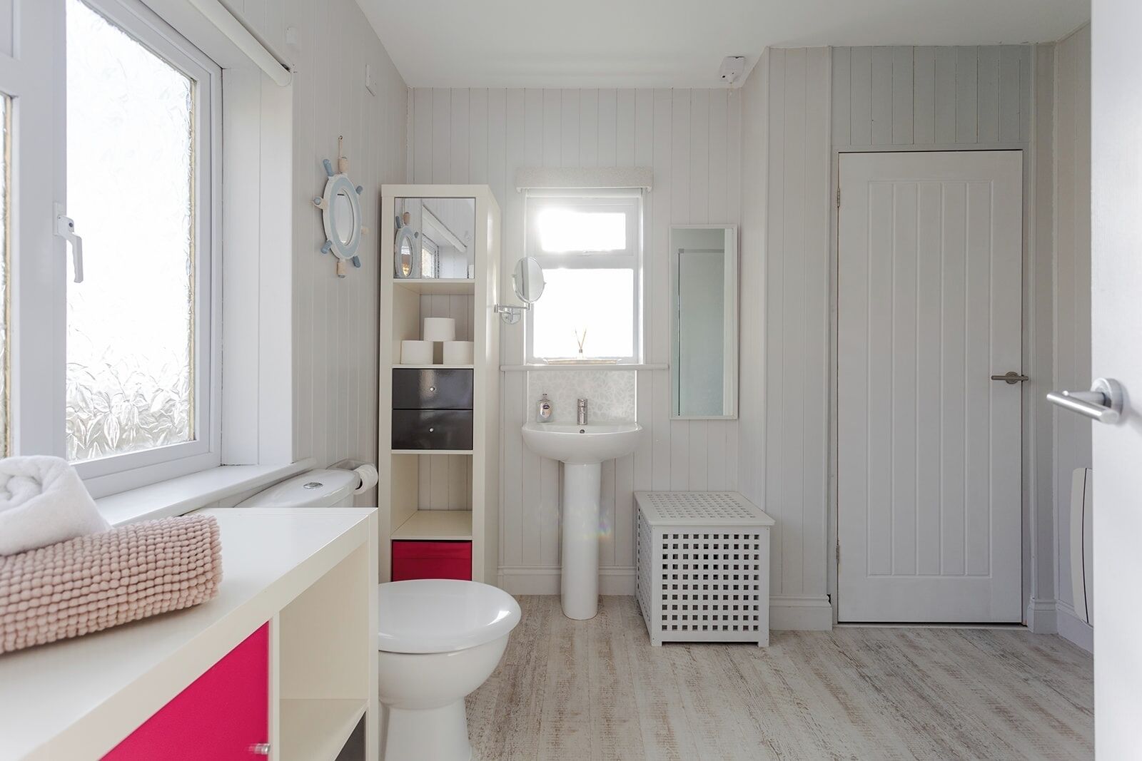 Un baño con inodoro, lavabo y estantes abiertos con artículos de aseo.