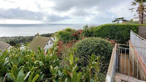 A coastal residential area with a view of the sea, a white house, and lush greenery.
