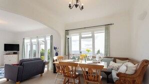 A spacious living area with a sofa, dining table, chairs, and a TV.