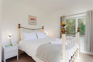 A bedroom with a four-poster bed, a bedside table with a lamp, a framed picture on the wall, and a window with curtains.