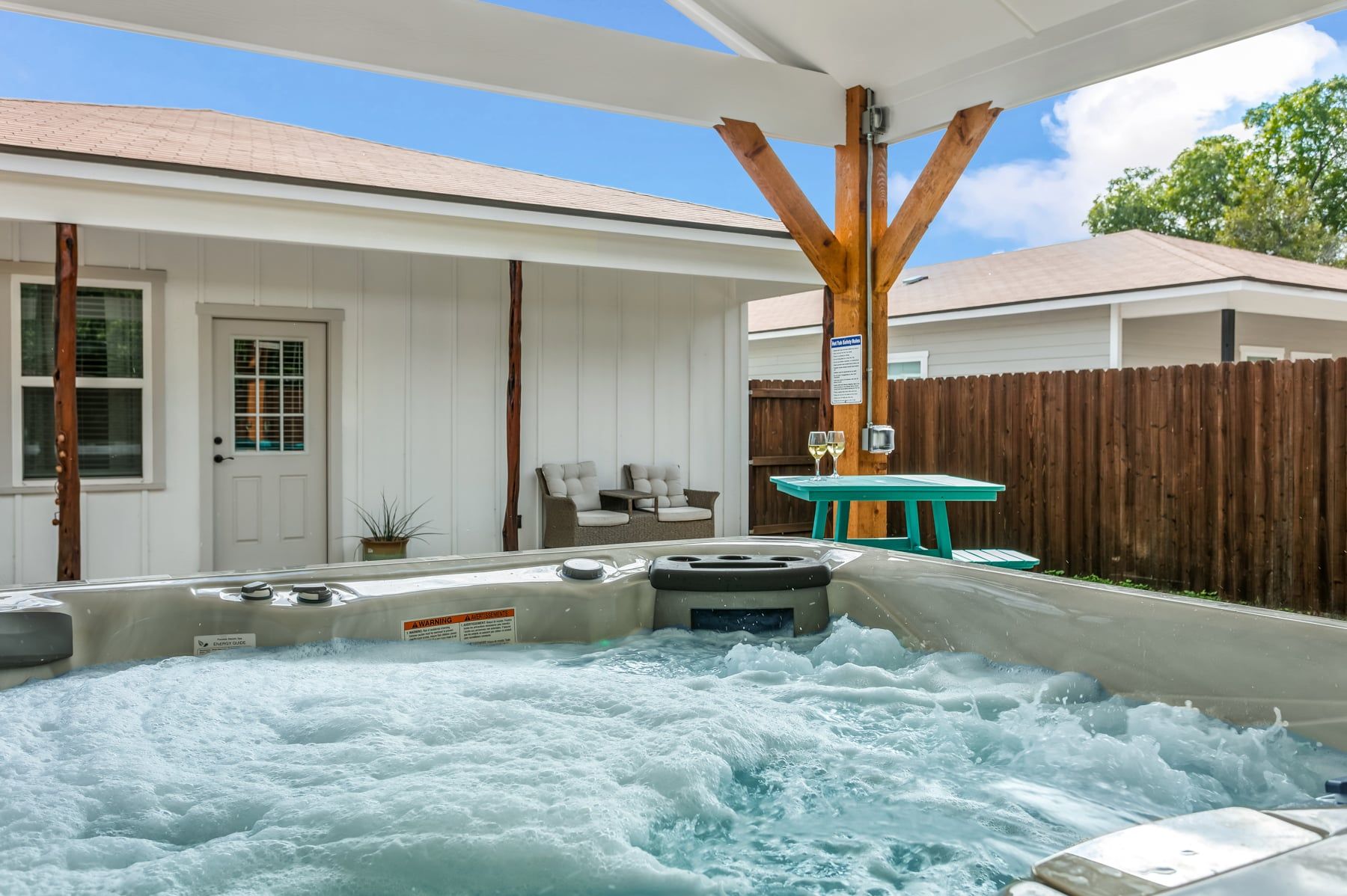 Un jacuzzi con una estructura de madera encima, una valla de madera y una casa con una puerta y ventanas al fondo.