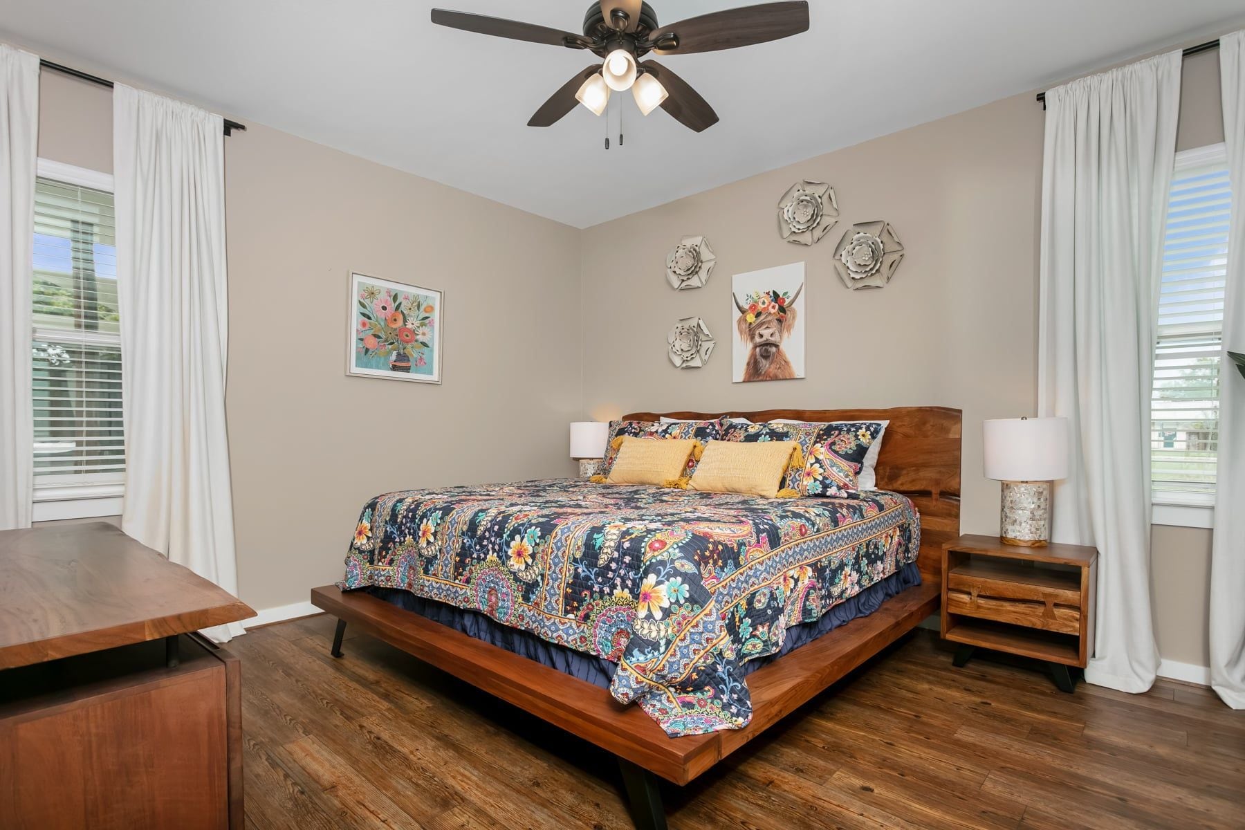 A bedroom with a bed, a nightstand, a ceiling fan, and decorative wall art.
