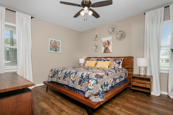 A bedroom with a bed, a nightstand, a ceiling fan, and decorative wall art.
