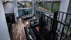 A spacious living area with a dining table set for six, a black leather sofa, and a staircase leading to an upper level. - Beartopia - Indoor Splashes, Scenic Hot Tub Soaks, Fireside Sips & Games Galore (Sevierville)