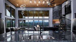 A modern kitchen with granite countertops, a stainless steel sink, and a large window overlooking a mountainous landscape. - Beartopia - Indoor Splashes, Scenic Hot Tub Soaks, Fireside Sips & Games Galore (Sevierville)