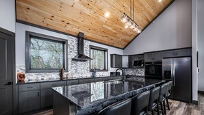 A modern kitchen with a large island, dark cabinetry, and a wooden ceiling. - Beartopia - Indoor Splashes, Scenic Hot Tub Soaks, Fireside Sips & Games Galore (Sevierville)