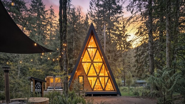 Une cabane triangulaire en bois, dotée d’une façade en verre, entourée d’une forêt.