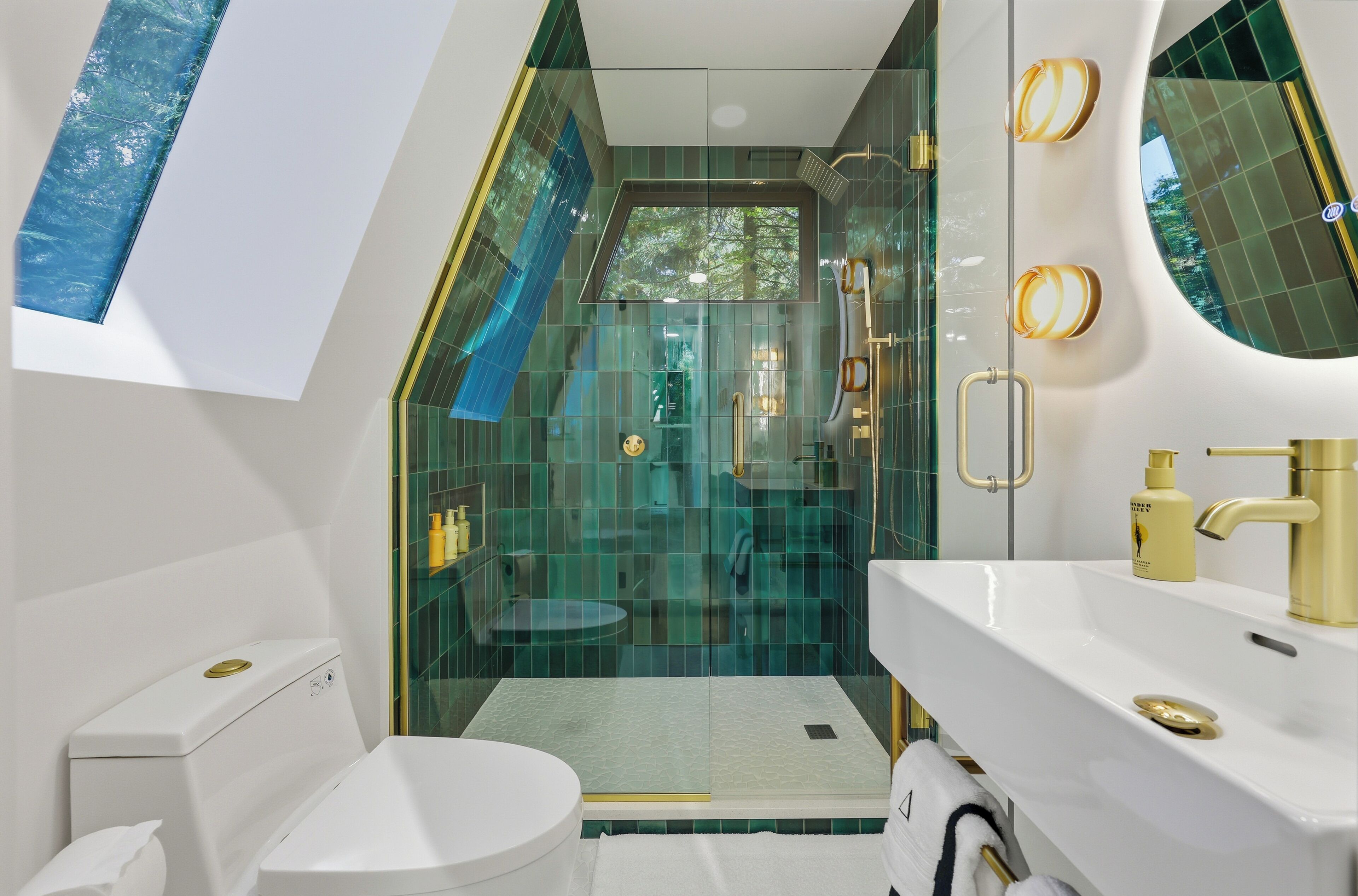 A modern bathroom with a glass-enclosed shower, a white toilet, and a gold-finished sink.