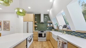 Une cuisine moderne dotée d’un îlot central, d’un four encastré et offrant une vue sur l’extérieur grâce à une grande fenêtre.