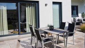 A modern house with a patio area featuring a table and chairs, a sliding glass door, and a satellite dish. - am Sonnenhang by Interhome (Attendorn)