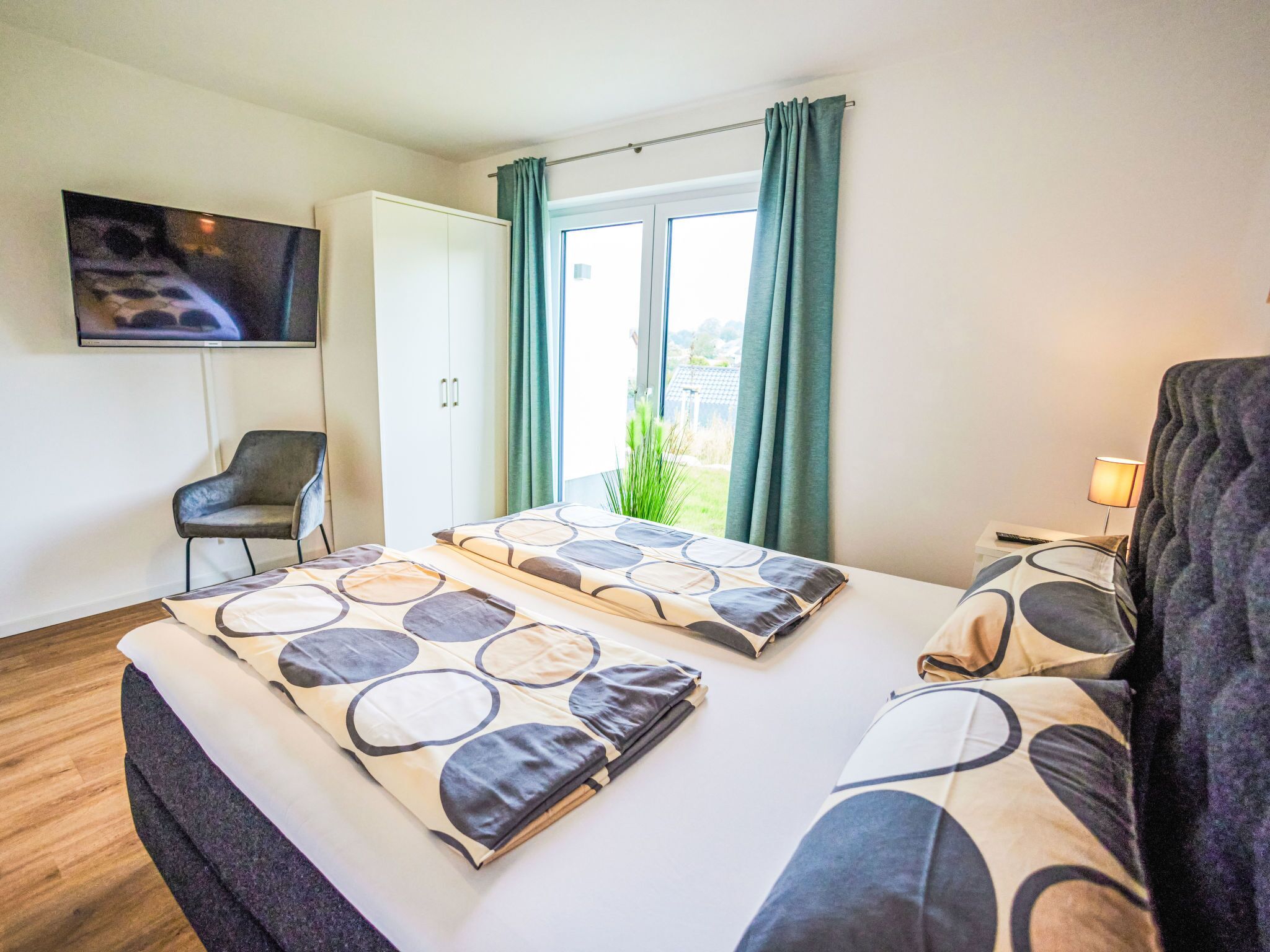 A hotel room with two beds, a TV, a chair, and a window with curtains.