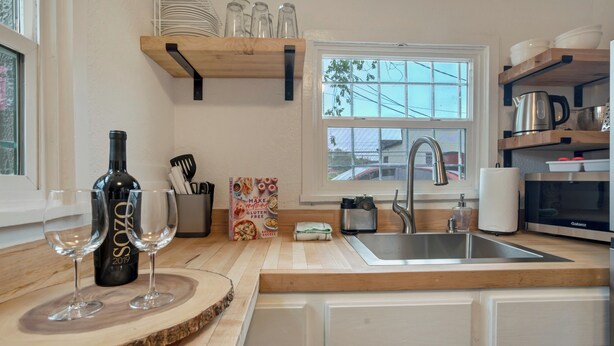 A kitchen with wooden countertops, a sink, a window, and shelves with dishes and a kettle. - Charming Downtown Cottage (Colorado Springs)