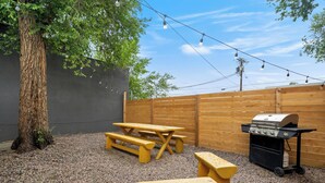 A backyard with a wooden fence, a tree, and a barbecue grill. - Charming Downtown Cottage (Colorado Springs)
