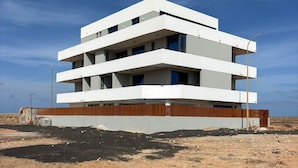 A modern multi-story building with a flat roof, large windows, and a wooden facade. - Joli Beach House - Spacious Ground Floor T2 Apartment (Sal)