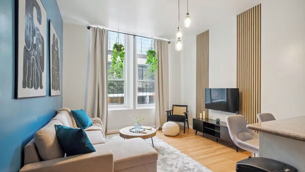 A modern living room with a sofa, a coffee table, a TV, and a dining area. - Modern  Bright 1-bedroom condo in Rittenhouse Square- Center City Philadelphia (Philadelphia)
