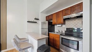 A modern kitchen with wooden cabinets, stainless steel appliances, and a bar stool. - Modern  Bright 1-bedroom condo in Rittenhouse Square- Center City Philadelphia (Philadelphia)